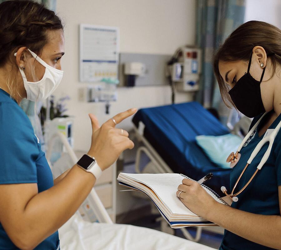 two nursing students talking while one student takes notes in a notebook